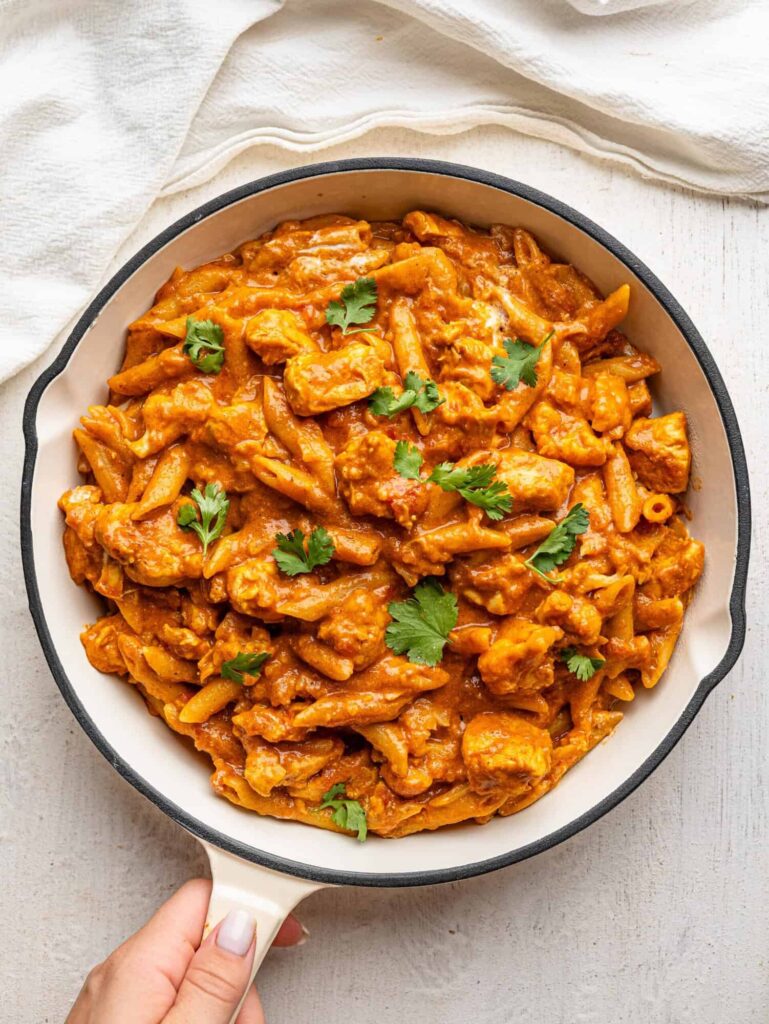 Butter chicken pasta cooking in a skillet with creamy tomato sauce